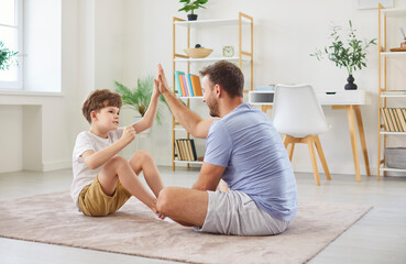 Father and son give each other a high five after a fitness workout at home. Strong family bonding...
