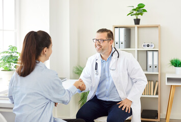 Smiling and happy doctor or nurse shakes hands with a female patient during visit to the hospital. Medical healthcare, trust, and professional care provided in the clinical environment.