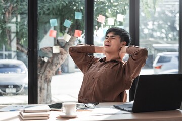 Man in Brown Shirt Stretching Neck at Work Station by Window