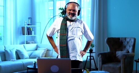 Indian senior man doing online exercise session using laptop in modern home interior, happy aged Asian male following virtual fitness routine indoors to stay healthy, active, and physically fit