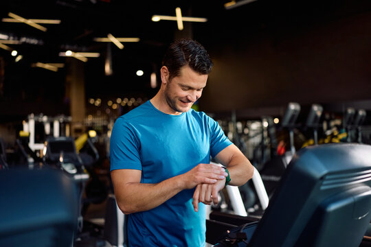 Happy athletic man using fitness tracker while exercising in gym.