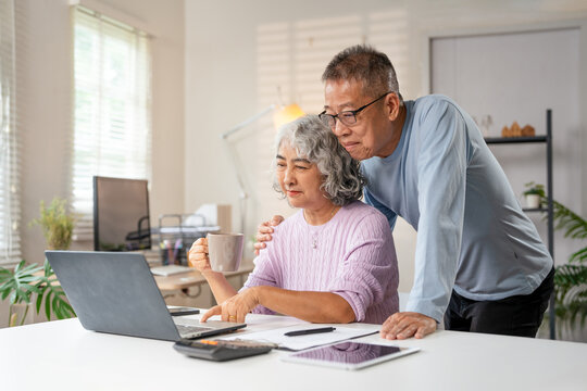 Senior Spouses enjoying retirement and free time browsing on laptop  At Home. Older Couple Browsing Internet On Computer Reading Online News On Weekend. Technology And Gadgets.