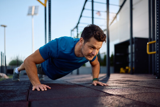 Athletic man doing push ups while exercising in outdoor gym.