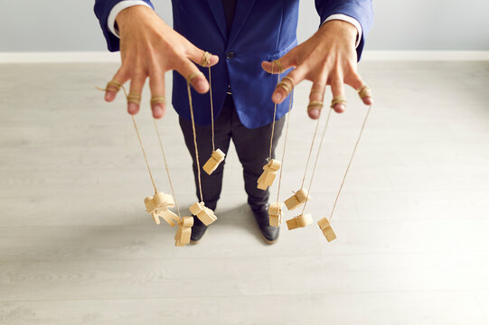 Businessman hands controlling wooden puppets or marionettes with strings on fingers, symbolizing people leadership, manipulation, and strategic decision making in business work operations.
