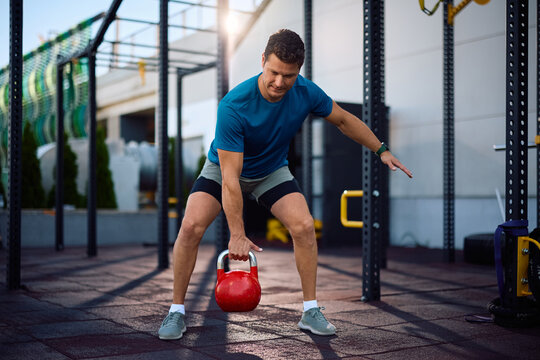 Male athlete exercising with kettlebell on cross training in outdoor gym.