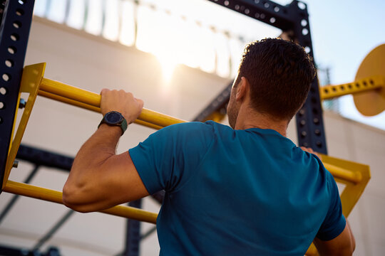 Rear view of sportsman practicing pull ups while working out in health club.