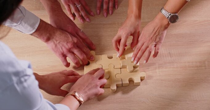 Group of business people assembling big wooden puzzle standing at the desk in office. Cooperation, teamwork and support concept. Coworkers join jigsaw pieces. 4k video. Slow motion video.
