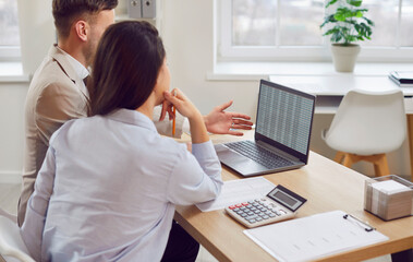 Business people looking at laptop screen together, back view. Man and woman in office checking...