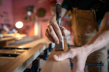 Woodworker hands examining wooden beams for uneven areas use chisel to smooth surfaces before...