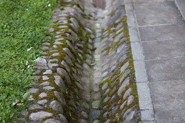 A brick drain alongside a sidewalk, often used for drainage purposes
