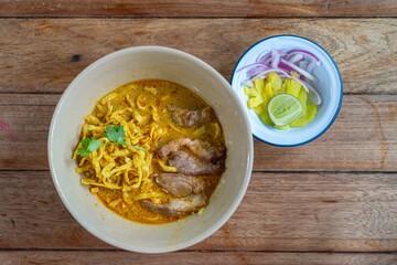 Khao Soi with fried pork served with pickled vegetables, onion, and lime. Traditional Northern Thai noodle curry dish.