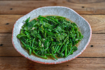 Stir-fried chayote leaves with garlic and oyster sauce on plate. Thai vegetable dish served on wooden table.
