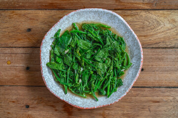 Stir-fried chayote leaves with garlic and oyster sauce on plate. Thai vegetable dish served on wooden table.