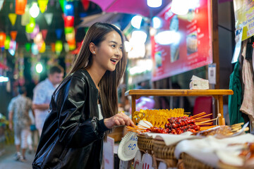 Asian woman enjoying street food at Chiang Mai Walking Street Night Bazaar. Young traveler exploring vibrant night market in Thailand.