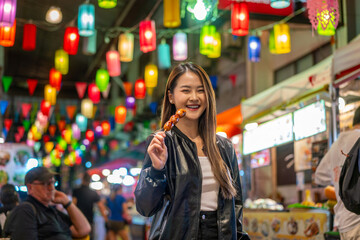 Asian woman enjoying street food at Chiang Mai Walking Street Night Bazaar. Young traveler exploring vibrant night market in Thailand.