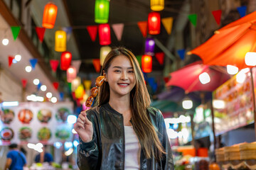 Asian woman enjoying street food at Chiang Mai Walking Street Night Bazaar. Young traveler exploring vibrant night market in Thailand.