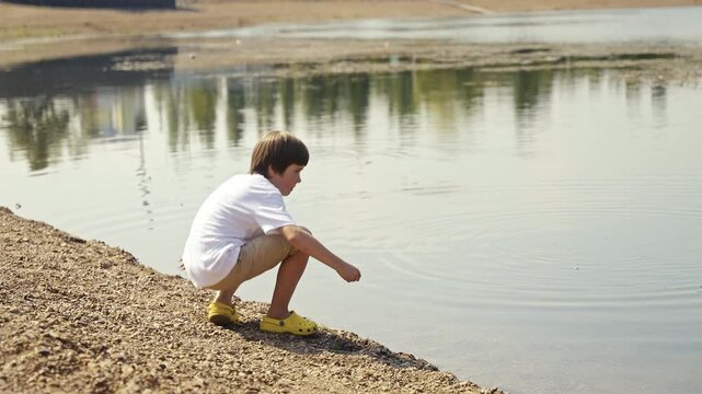 A joyful child delights at the waters edge, skipping stones and exploring nature on a bright sunny day