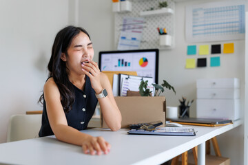 Tired asian office worker yawning at workplace desk