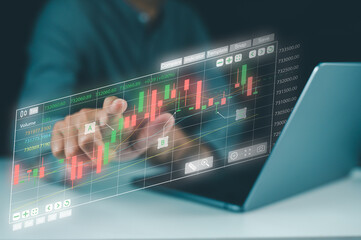 A person interacts with a transparent digital stock market chart projected above a laptop, analyzing financial data with candlestick graphs.