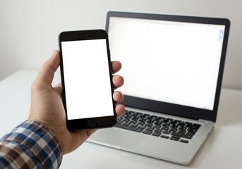 Hand Holding Smartphone with Blank Screen, Laptop in Background