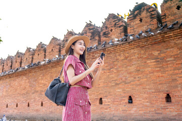 Asian woman using phone while exploring Tha Phae Gate in Chiang Mai. Young female tourist enjoying...