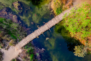 Aerial Bamboo Bridge Over River With Algae - Natural Top View - Aerial view of a rustic bamboo footbridge crossing a shallow green river with visible underwater algae. Captured with drone in rural Ind