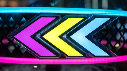 Neon arrows in vivid pink, yellow, and blue glow brightly against a dark arcade background, creating a vibrant and modern visual aesthetic with retro vibes.