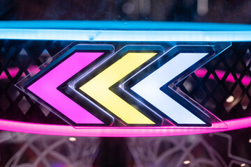 Neon arrows in vivid pink, yellow, and blue glow brightly against a dark arcade background,...