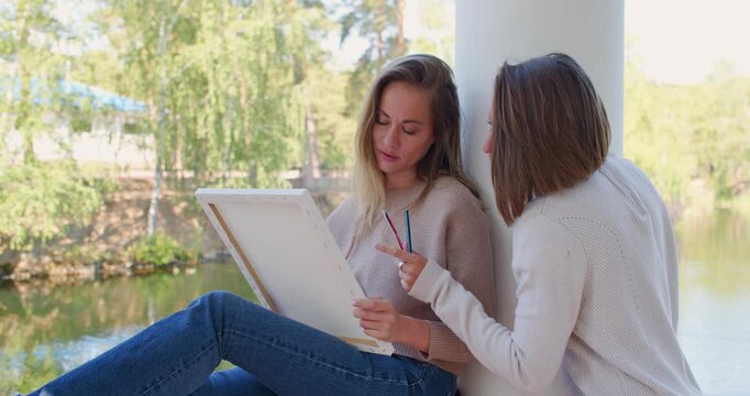Love and self-expression through art - women paint outdoors. Lesbian couple painting portraits of each other outdoors. Psychological relief through communication and art. Slow motion 4k footage.