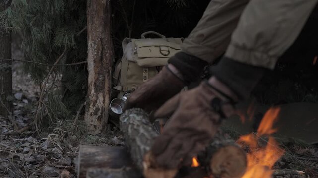 A man prepares firewood in a shelter for survival in the forest, a wildlife survivalist arranges logs near a makeshift shelter using gloves in the cold forest
