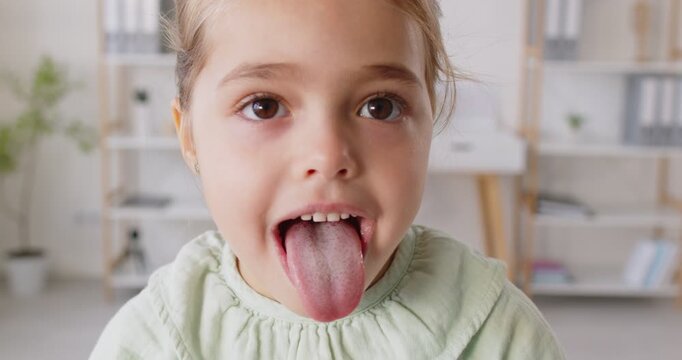 Close-up portrait captures a child patient showing her tongue during a dental or throat inspection in a clinic. The scene highlights child healthcare, dentistry, and a thorough medical check up. - Powered by Adobe
