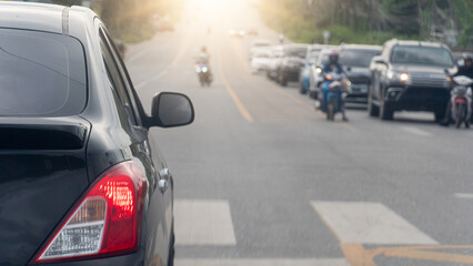 Rear side of black car with turn on brake light. Parked at the intersection. Crosswalk in front. Cars on the opposite side are lined up. Ready to drive on the asphalt road leading to the hill ahead.