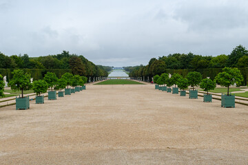 This wide gravel path and potted trees in the gardens of the Palace of Versailles reflect the...