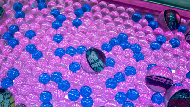 Brightly lit arcade prize balls with "100 tickets" text, surrounded by glossy blue and pink spheres under neon lighting, creating a fun, vibrant, and colorful game machine background.