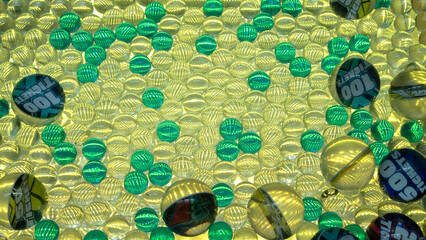 Colorful arcade game balls with shiny textures and embedded ticket values like 100, 500, and 50 tickets, scattered under bright lighting in a fun gaming environment.