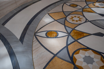 A detailed geometric pattern with circular and eye-like designs on a polished stone floor,...