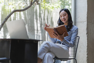 Young woman reading a book and using laptop in a cafe