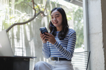 Young asian freelancer woman using mobile phone and laptop in cafe