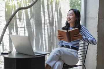 Young student reading a book and using laptop in modern library