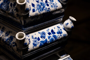Stacked blue and white floral ceramic pieces with intricate designs, set against a dark backdrop,...