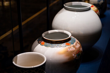 Colorful ceramic jars are displayed on a blue surface, each featuring intricate patterns and designs, under soft lighting in an indoor setting