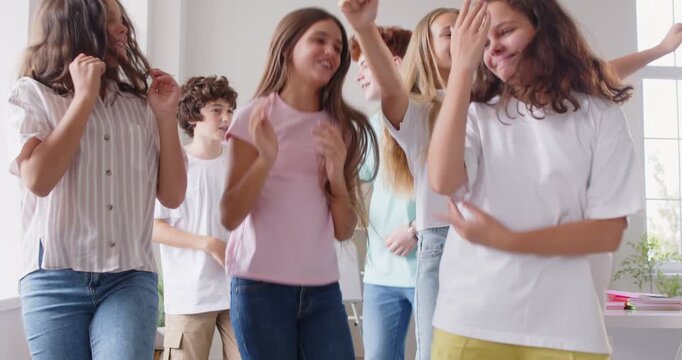 Cheerful caucasian high school children joyfully dancing in classroom during school break. Group of happy preteen classmates or friends enjoying relaxed atmosphere, laughing and having fun together.