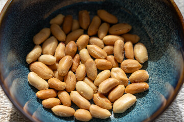 Bowl of roasted peanuts on textured surface