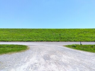 初夏の江戸川河川敷の駐車場に入る砂利道と若草生える土手風景