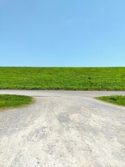 初夏の江戸川河川敷の駐車場に入る砂利道と若草生える土手風景