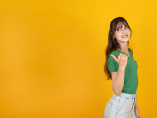 Pointing thumb finger back, young caucasian smiling excited brunette 20s woman pointing thumb...
