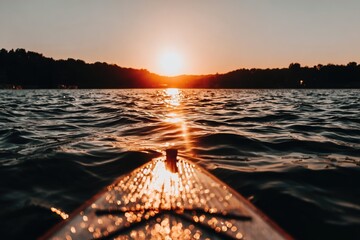 Sunset paddleboard view. A serene lake scene at sunset, seen from the front of a paddleboard. Ripples on the water, golden light reflecting on the water and board. Silhouette of distant trees
