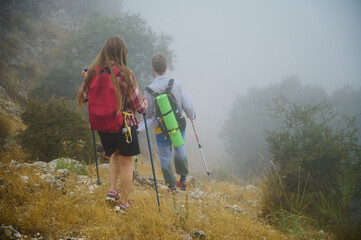 Couple Hiking Through Misty Mountain Trail with Backpacks and Trekking Poles