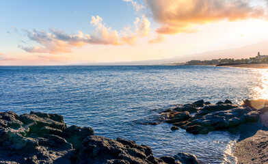 black rock sea beach during sunrise or sunset with golden sand, mild surf, blue calm water and...
