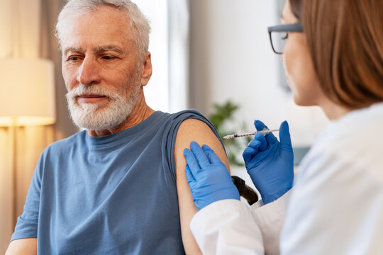 Doctor giving vaccine injection to senior man at home